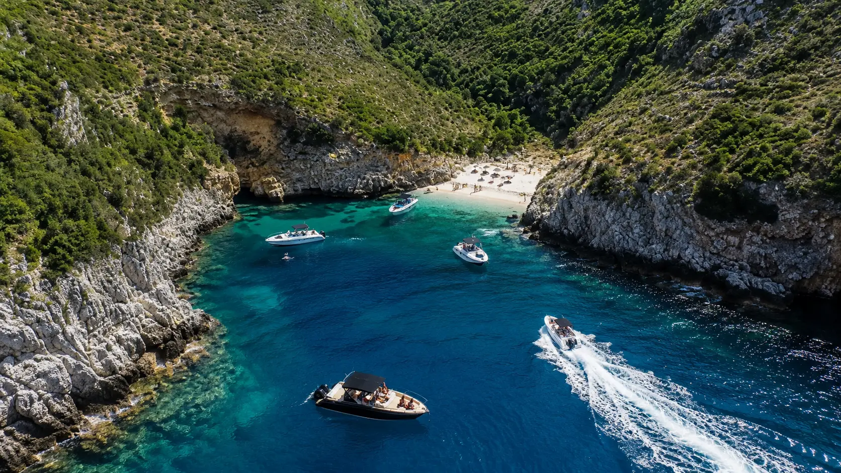 Aerial view of Dafina Bay in Albania with crystal-clear turquoise water, modern speedboats and tourists enjoying the Albanian Riviera.