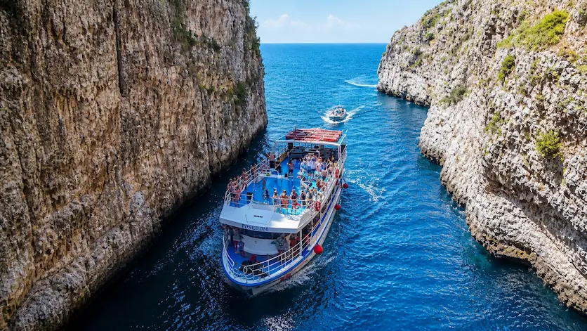 Large boat tour cruising between sea cliffs with tourists on board along the Albanian Riviera