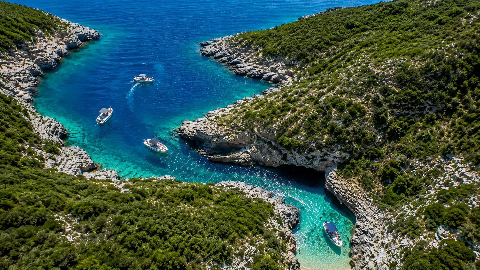 Aerial panoramic view of Englishman Bay in Karaburun, Albania with crystal-clear turquoise water, rocky cliffs and tourist boats.