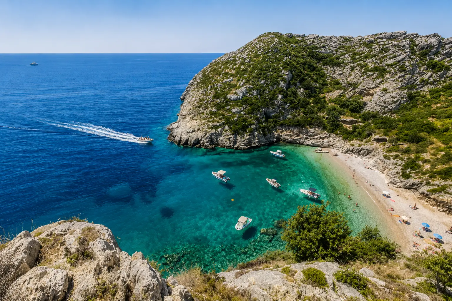 Aerial view of Grama Bay in Albania with turquoise water, tourist boats and beach visitors enjoying the Albanian Riviera.