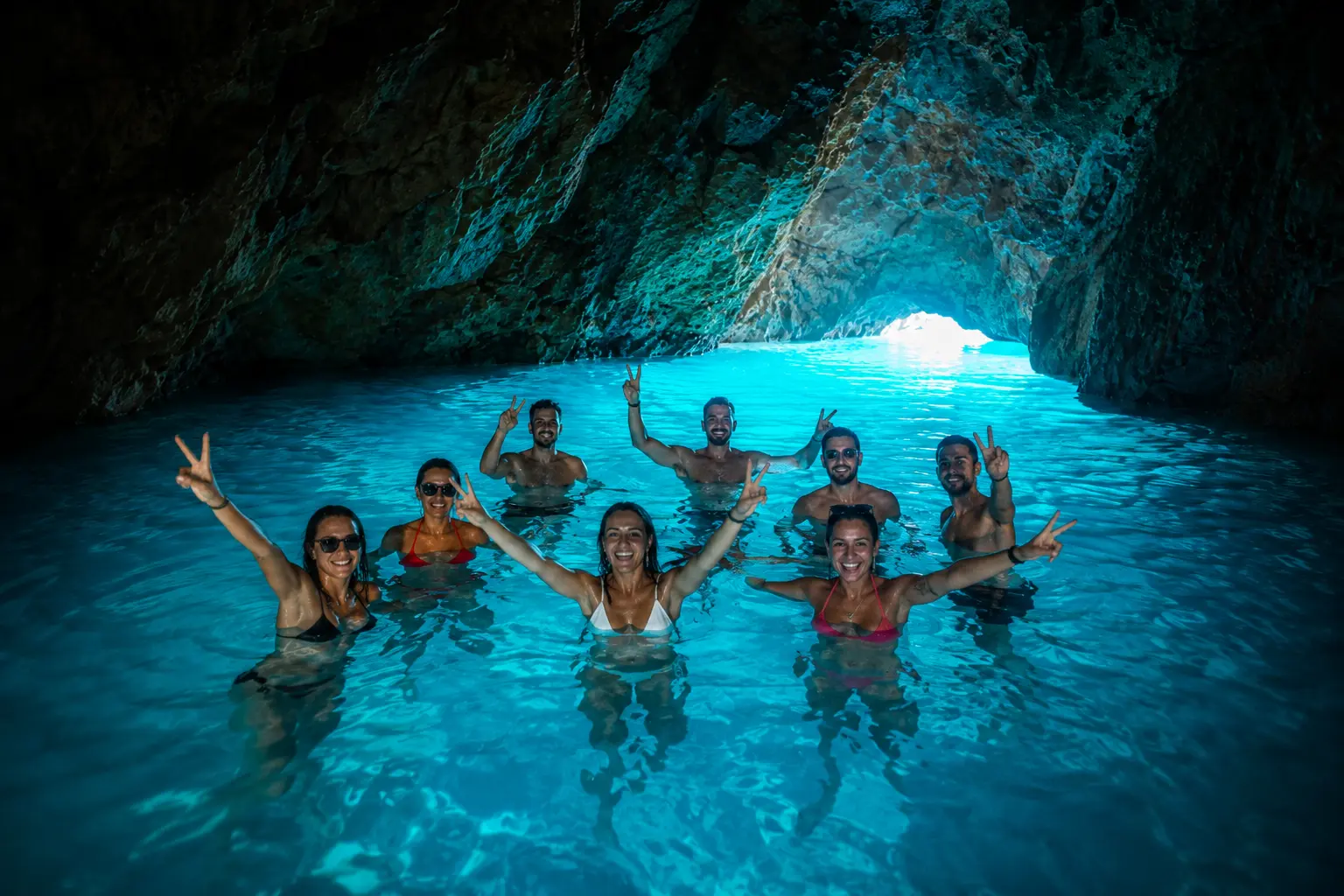 Tourists swimming inside the Secret Blue Cave in Albania with glowing turquoise water and natural cave reflections.